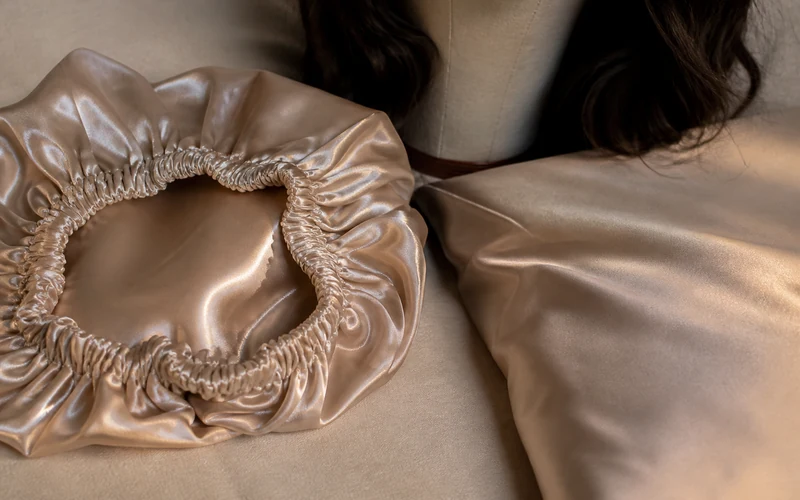 Satin bonnet and satin pillowcase beside a sheitel resting on a bedside canvas stand at night