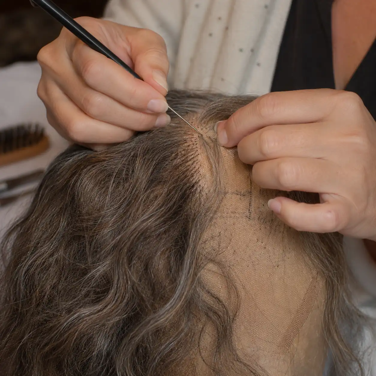 Artisan hand-tying hair into a wig foundation at a production workbench