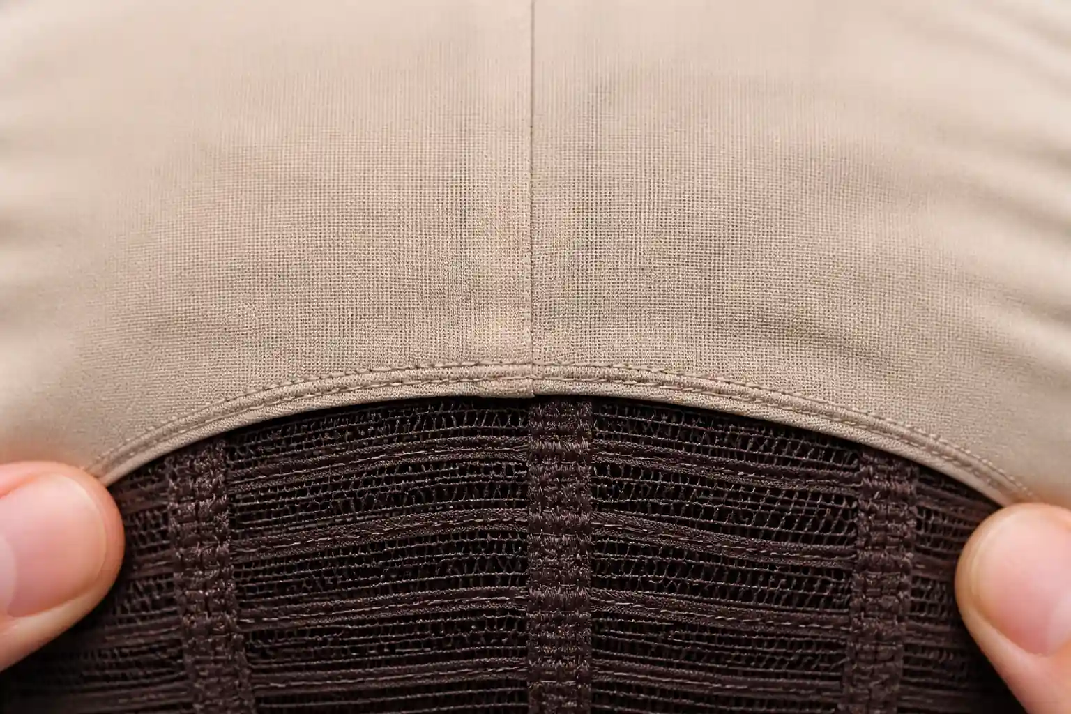 Illustrative inside close-up of the stitched junction between a pale silk crown panel and darker supporting mesh and weft rows